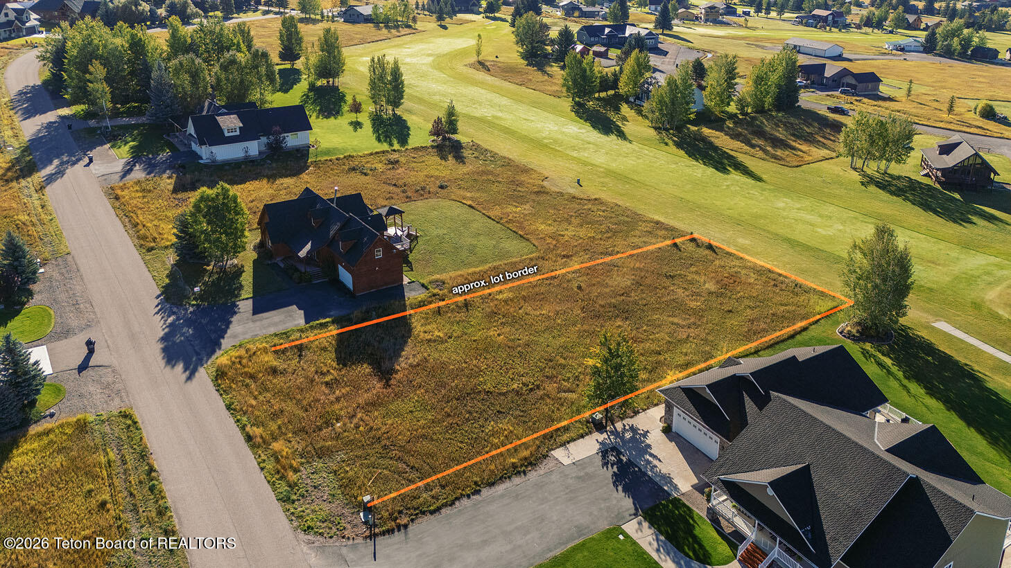 Vacant lot outlined beside a golf course and paved road.