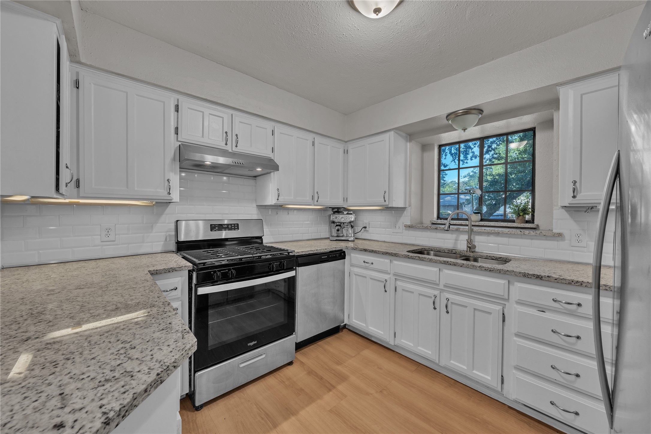 Kitchen with white cabinets, granite counters, stainless appliances, and a sink beneath a large window.