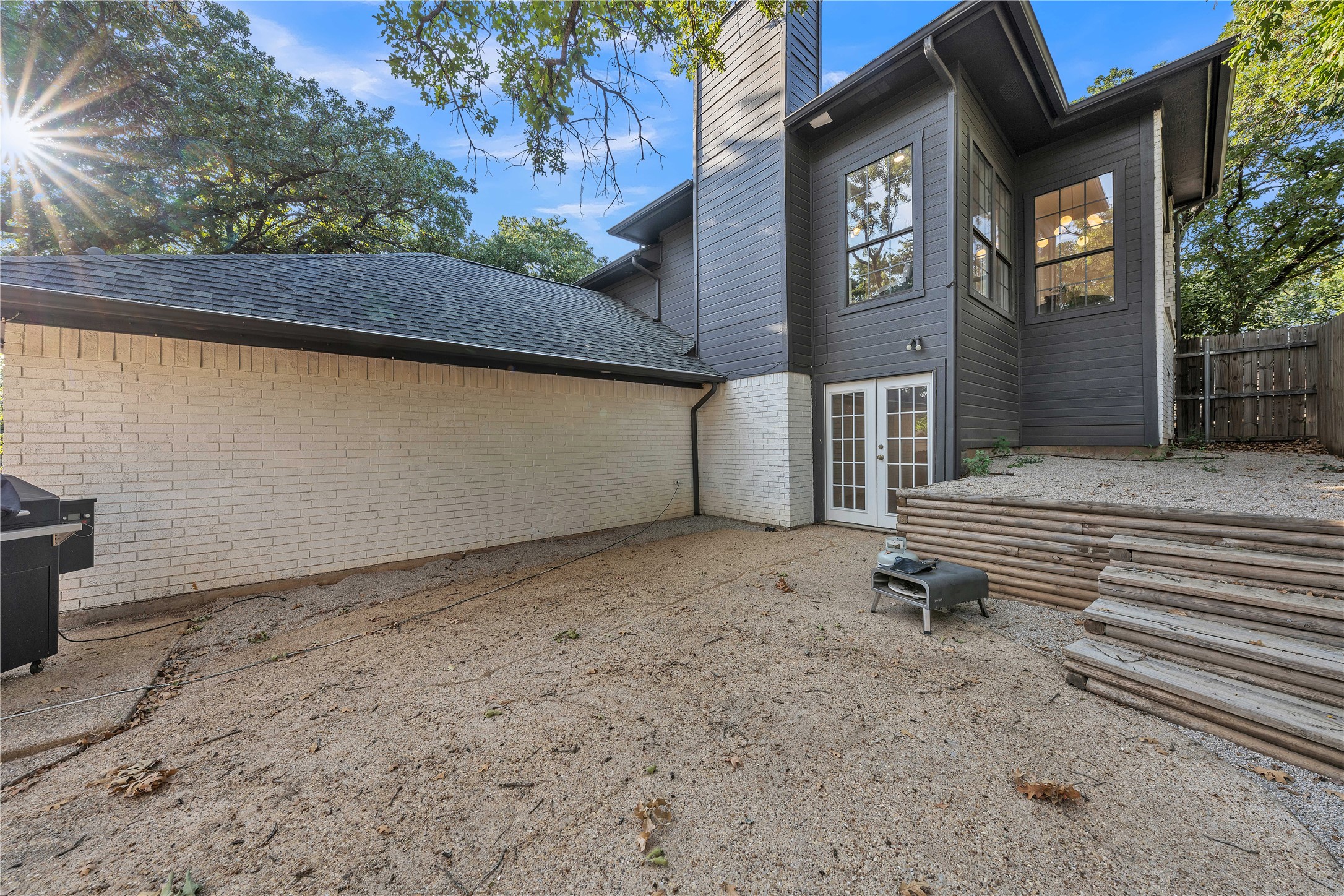 House’s rear exterior with French doors, a gravel patio, and a raised timber retaining wall.