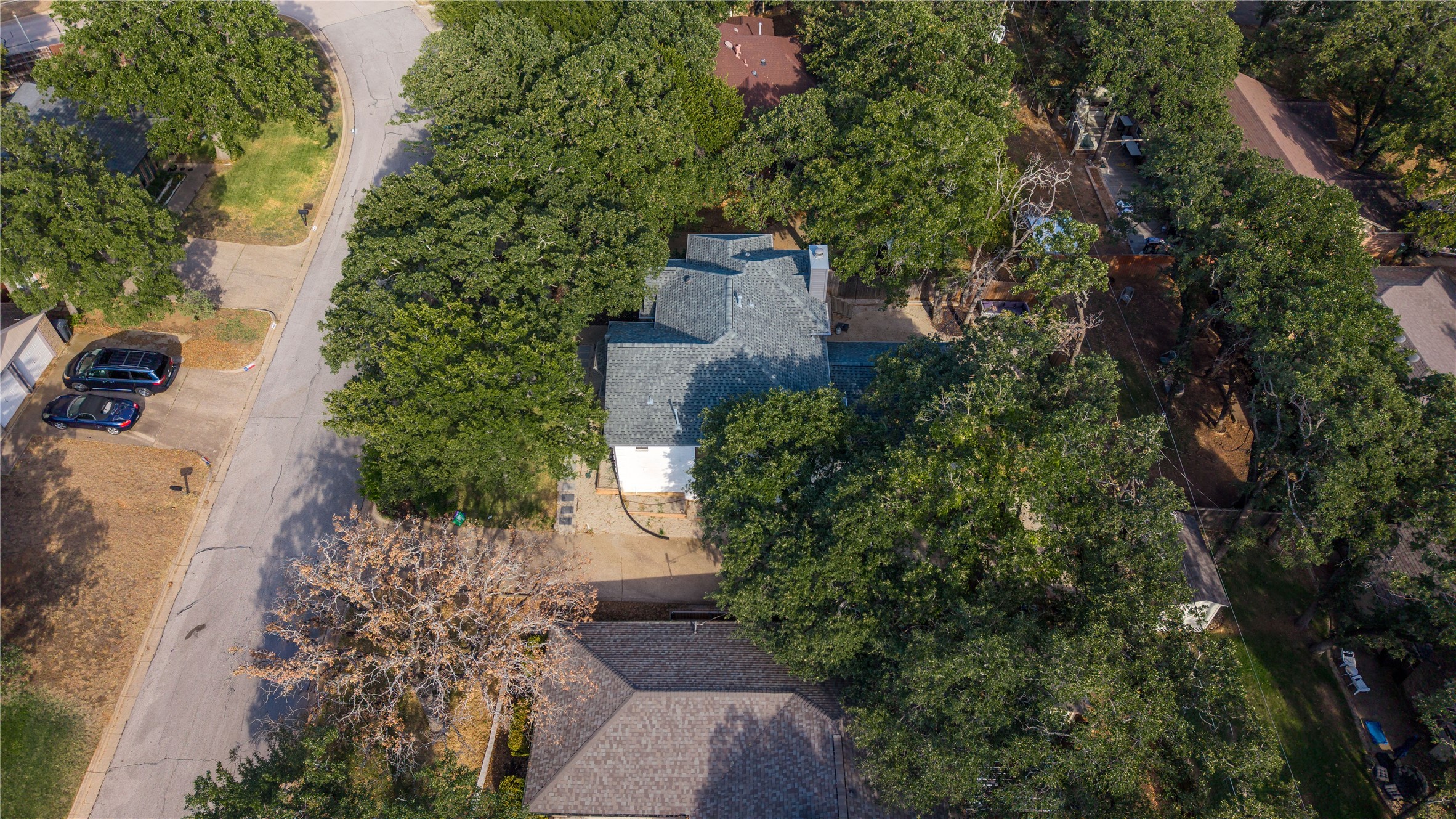 Aerial view of a gray-roofed house surrounded by mature trees and neighboring homes.