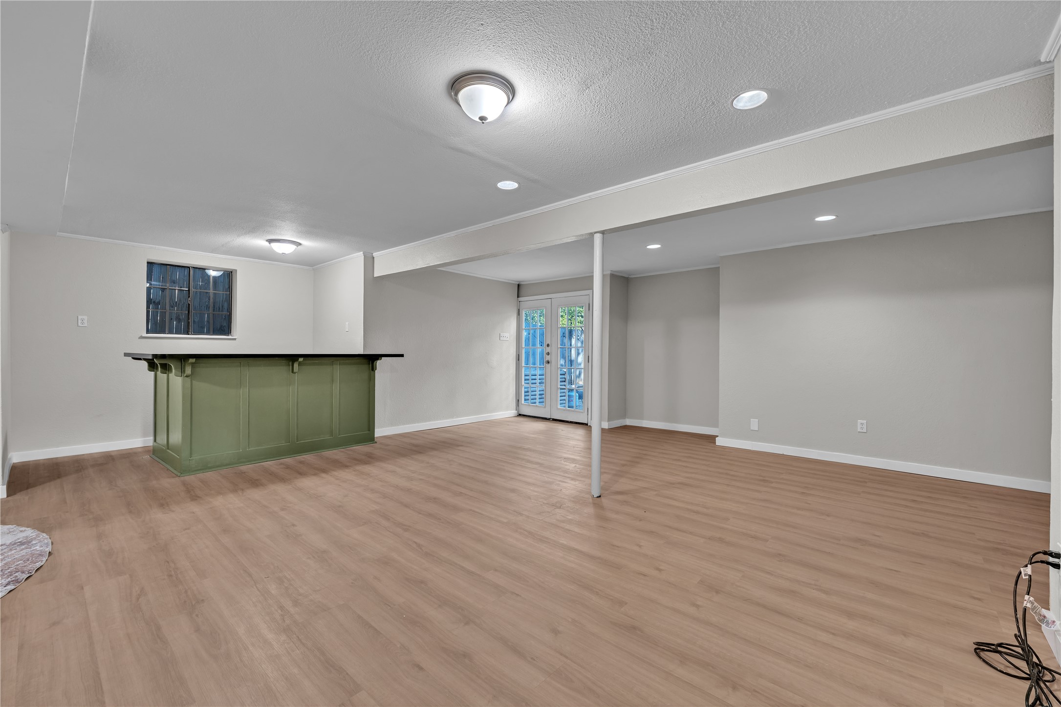 Empty room with wood-look flooring, a green bar, and glass-paneled French doors.