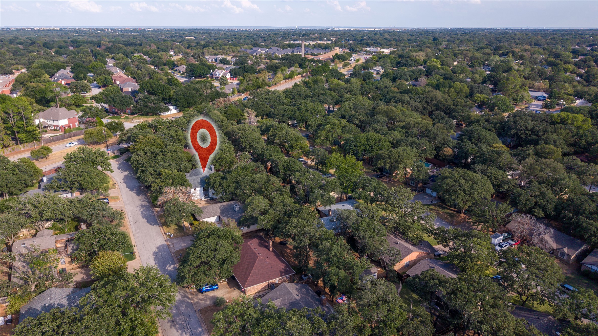 Aerial view of a leafy neighborhood, with a red pin marking the property among nearby homes.