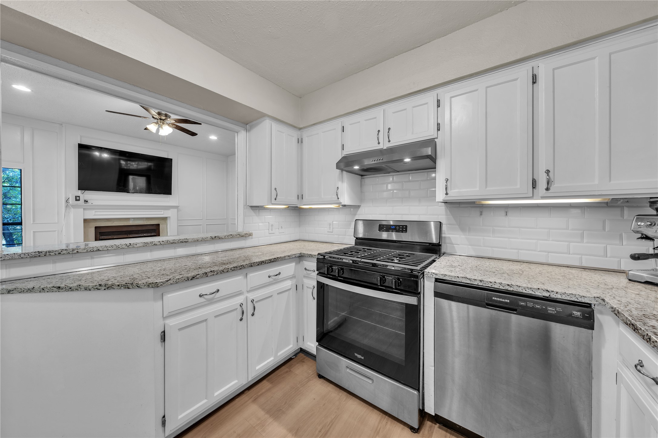 Kitchen with white cabinetry, granite counters, stainless appliances, and a pass-through to a living room.