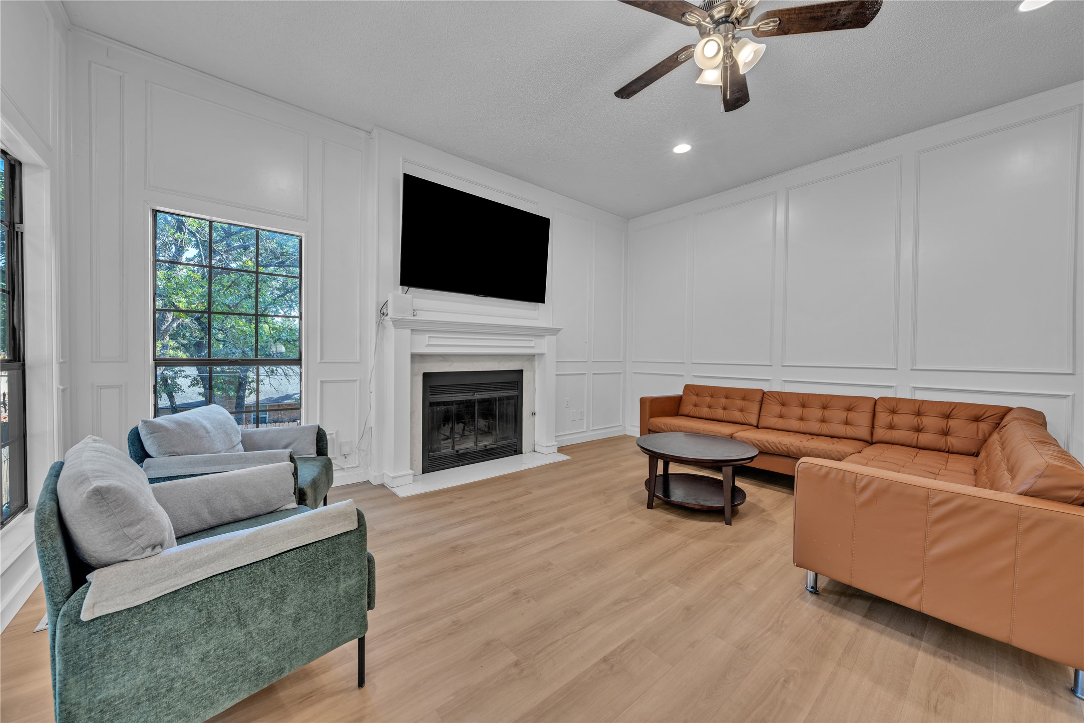 Living room with a fireplace, large windows, tan sectional, and green armchairs.