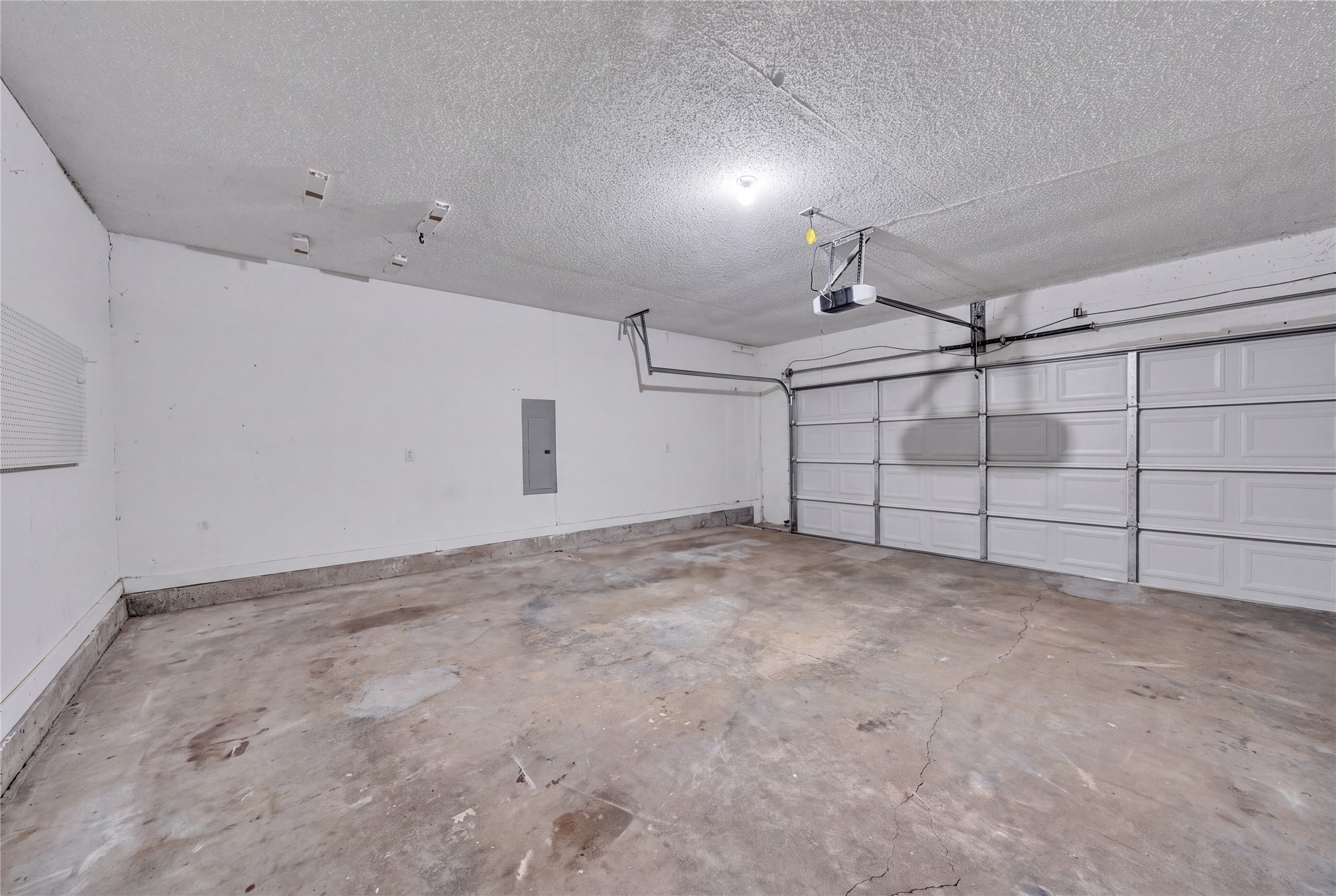 Empty garage with a concrete floor, white sectional door, and ceiling-mounted opener.