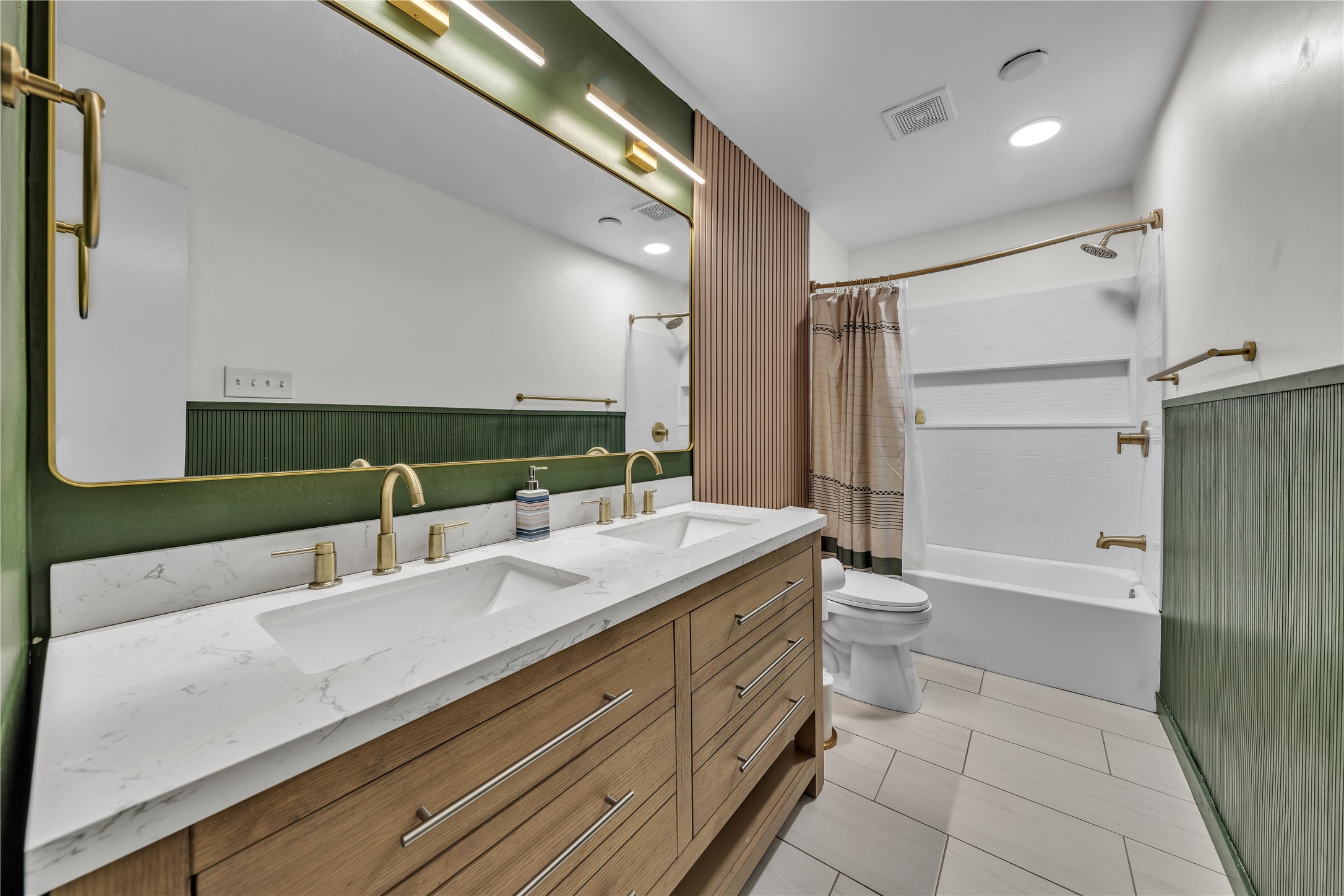 Bathroom with double wood vanity, brass faucets, green wainscoting, and a white tub-shower.