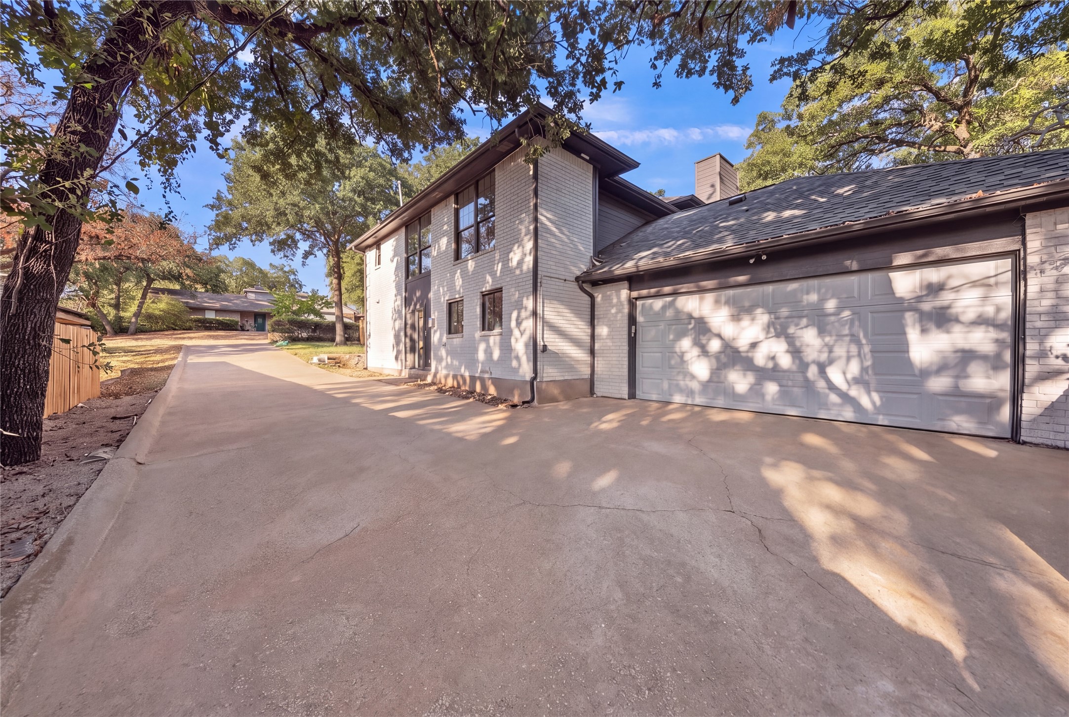 Two-story house with a double garage and wide driveway beneath mature trees.