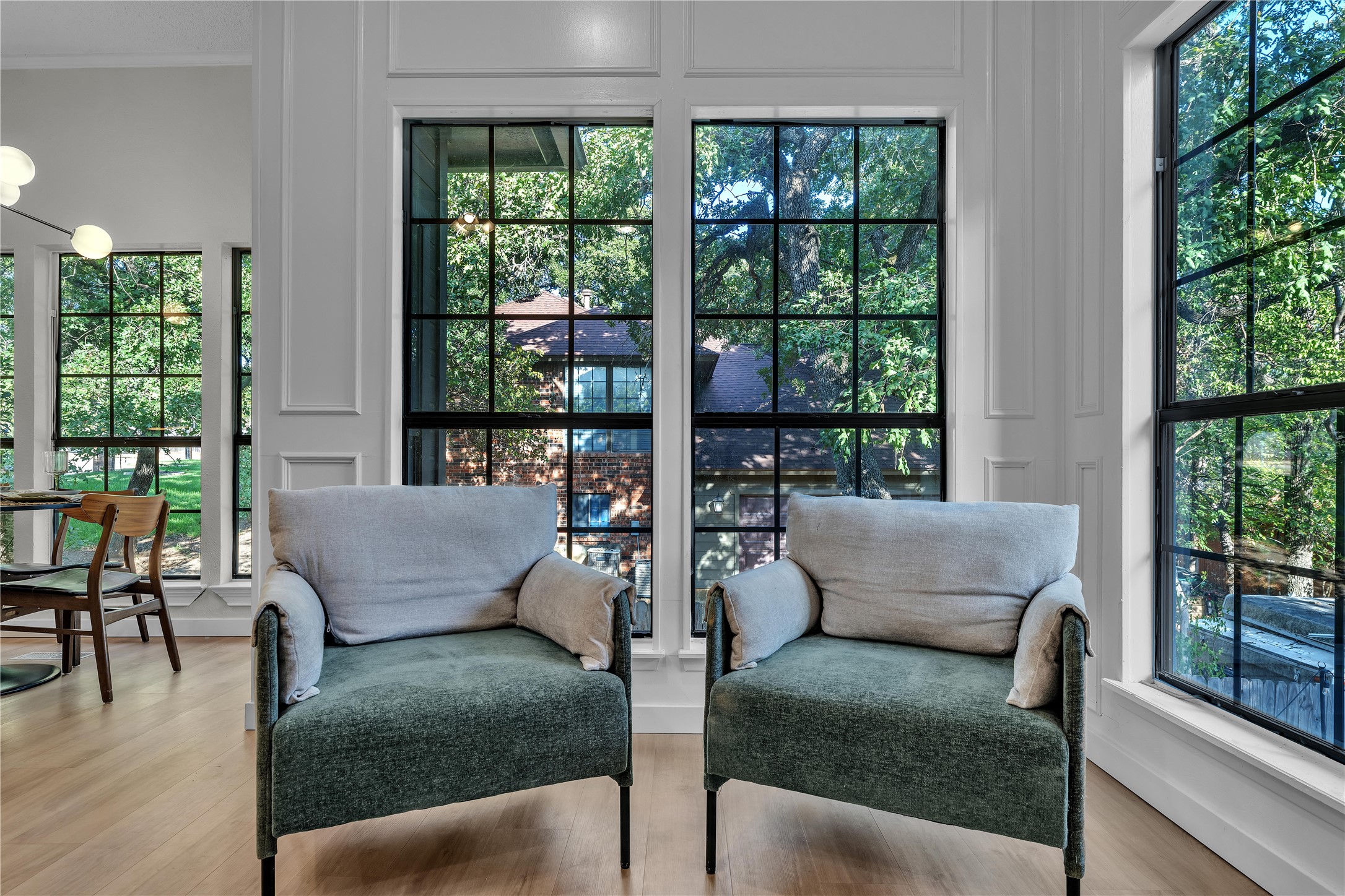 Living room with two upholstered armchairs and tall windows overlooking leafy trees.