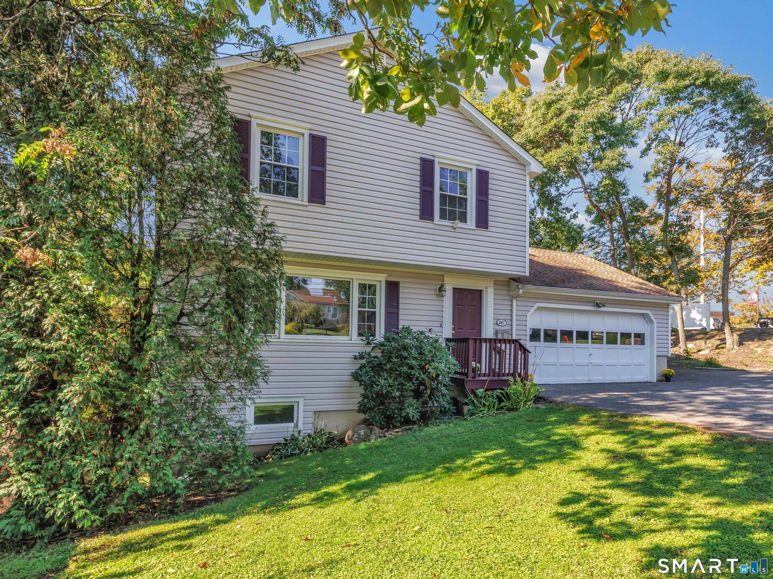 Two-story light-sided home with an attached garage, burgundy front door, and leafy lawn.