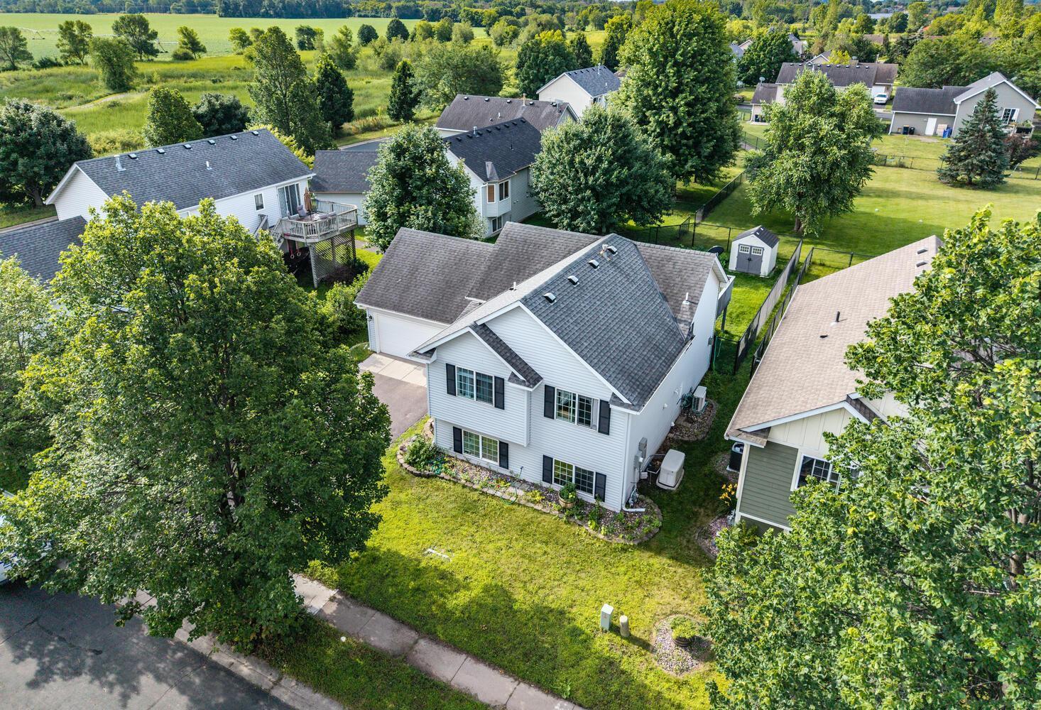Aerial view of a white two-story house with a gray roof, lawn, and mature trees.