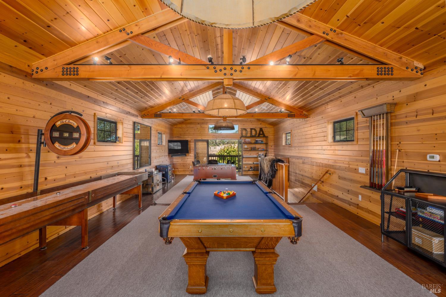 Wood-paneled game room with a blue pool table, shuffleboard, foosball table, and exposed timber beams.