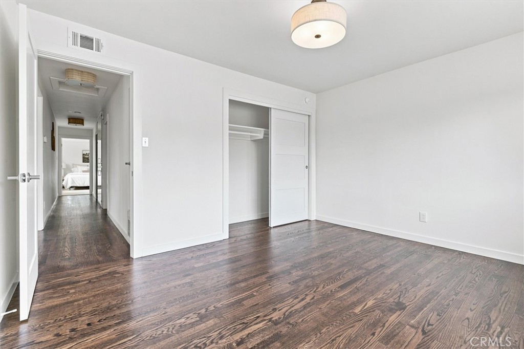 Empty bedroom with dark hardwood floors, a sliding-door closet, and a hallway leading to another bedroom.