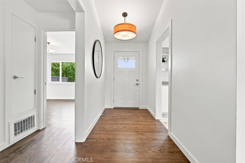 Bright entry hallway with dark wood floors, a white front door, and an orange pendant light.