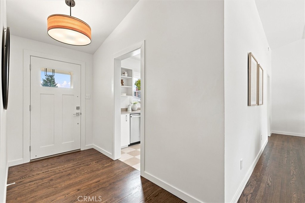 Bright entryway with a white front door, hardwood floors, and a view into the kitchen.