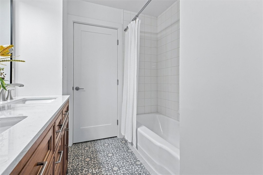 Bathroom with a wood vanity, patterned floor, and white tub-shower enclosure.