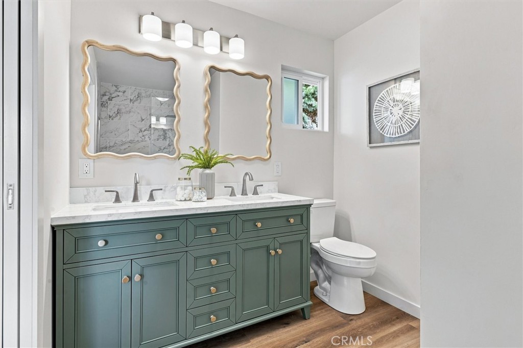 Bathroom with a green double vanity, marble countertop, decorative mirrors, and a toilet.