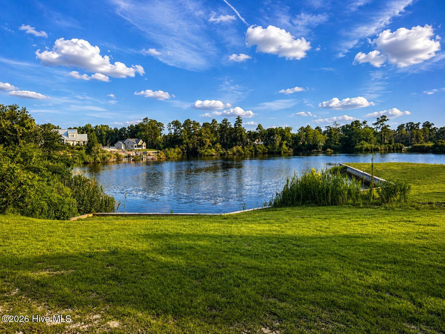 Waterfront view across a calm inlet from a broad grassy lawn and small dock.