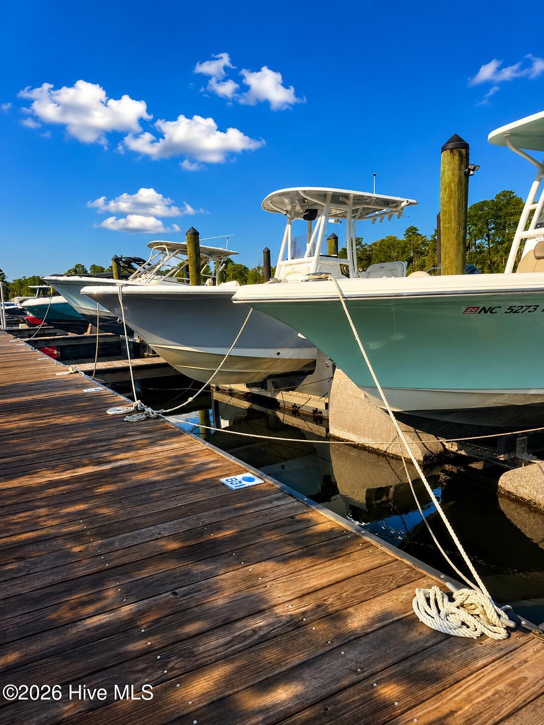 Motorboats tied beside a wooden dock, with tall pilings and a tree-lined shore.