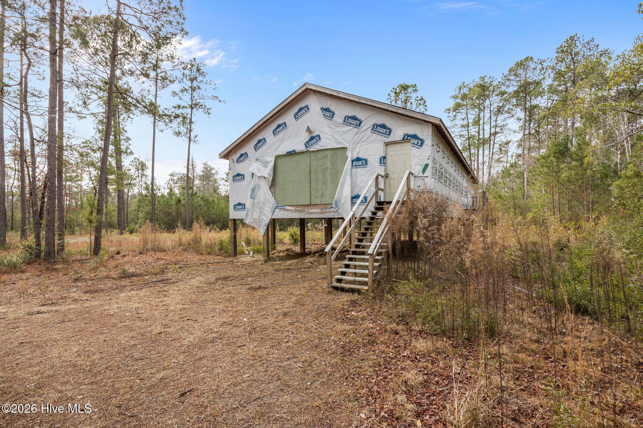 Elevated home under construction in a wooded clearing, with building wrap and temporary front stairs.
