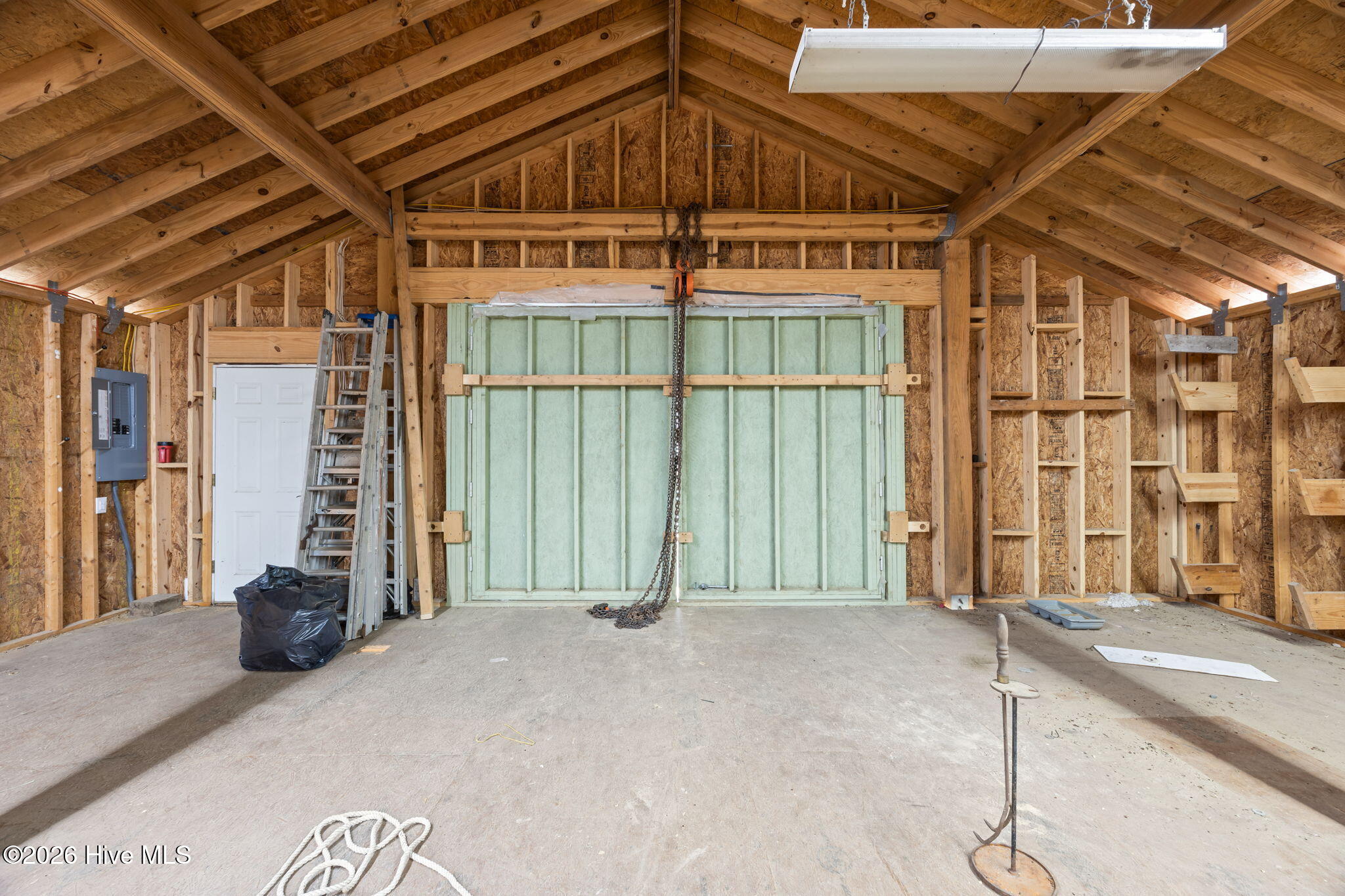 Unfinished garage with exposed timber framing and a wide pale green garage door.