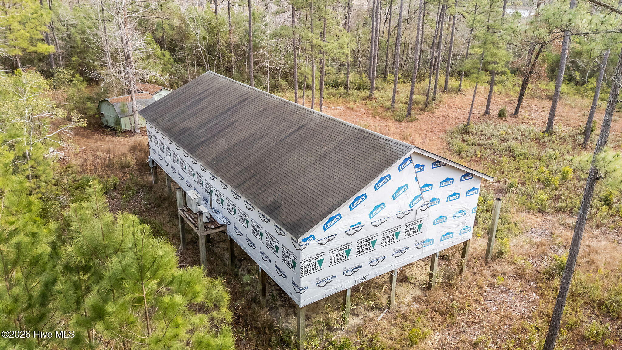 Aerial view of a wooded lot with a house under construction and a completed shingle roof.