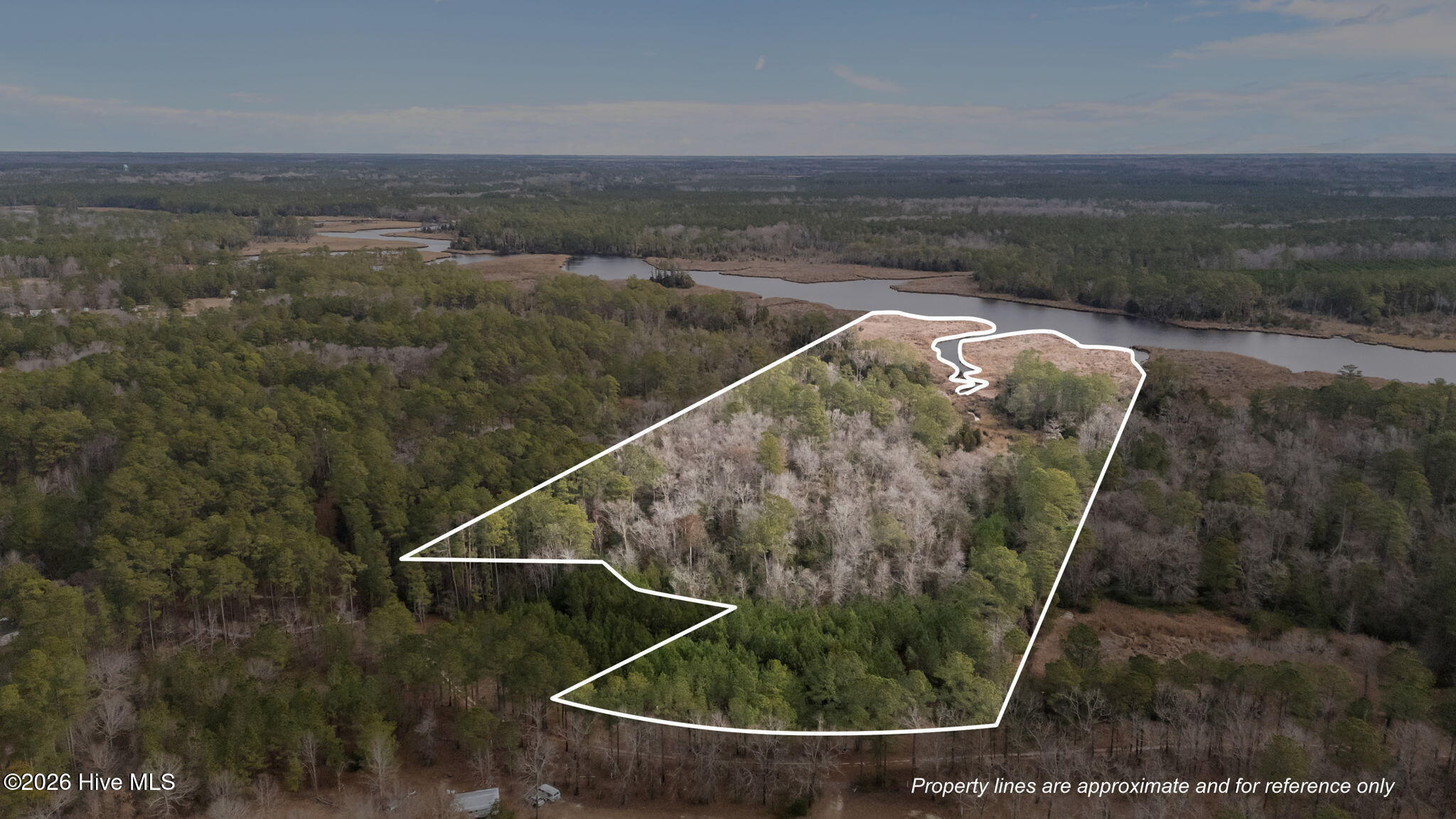 Aerial view of a wooded property outlined beside a winding waterway and marshland.