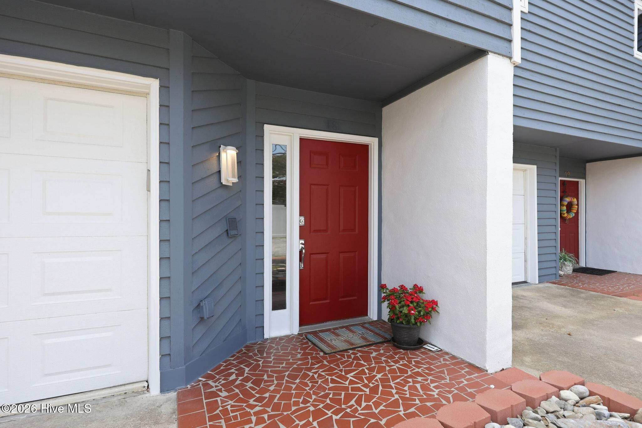 Townhouse entrance with a red door, blue siding, and a mosaic-tiled porch.