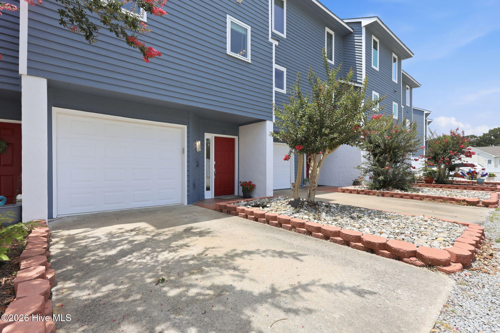 Blue townhouse exterior with a white garage door, red front door, and landscaped driveway.