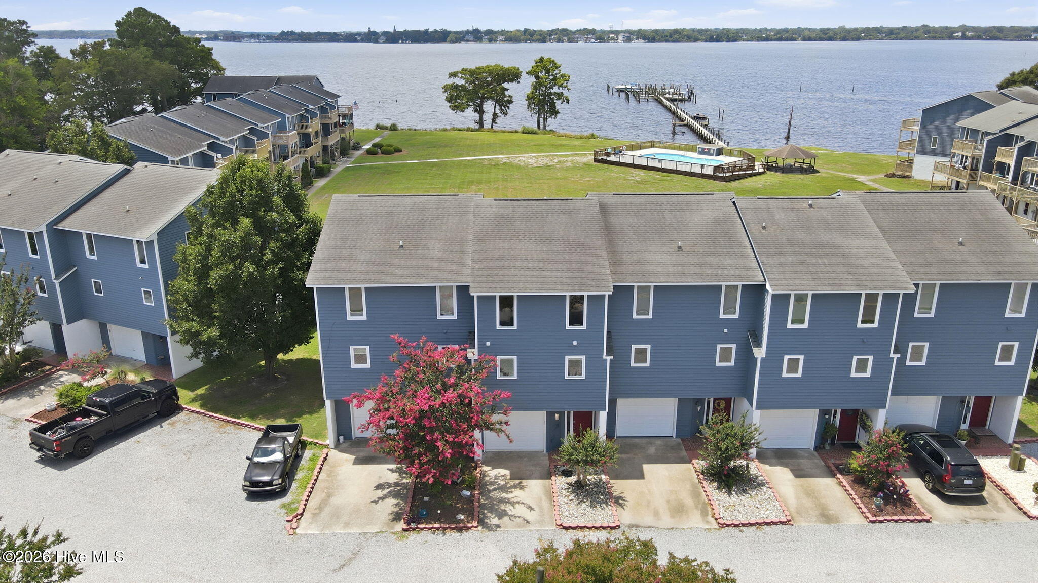 Waterfront townhouses beside a shared pool and gazebo, with a long dock extending into the water.