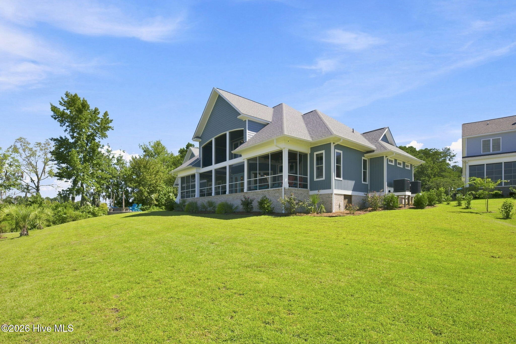 Blue-gray house with a large screened porch overlooking a broad, green lawn.