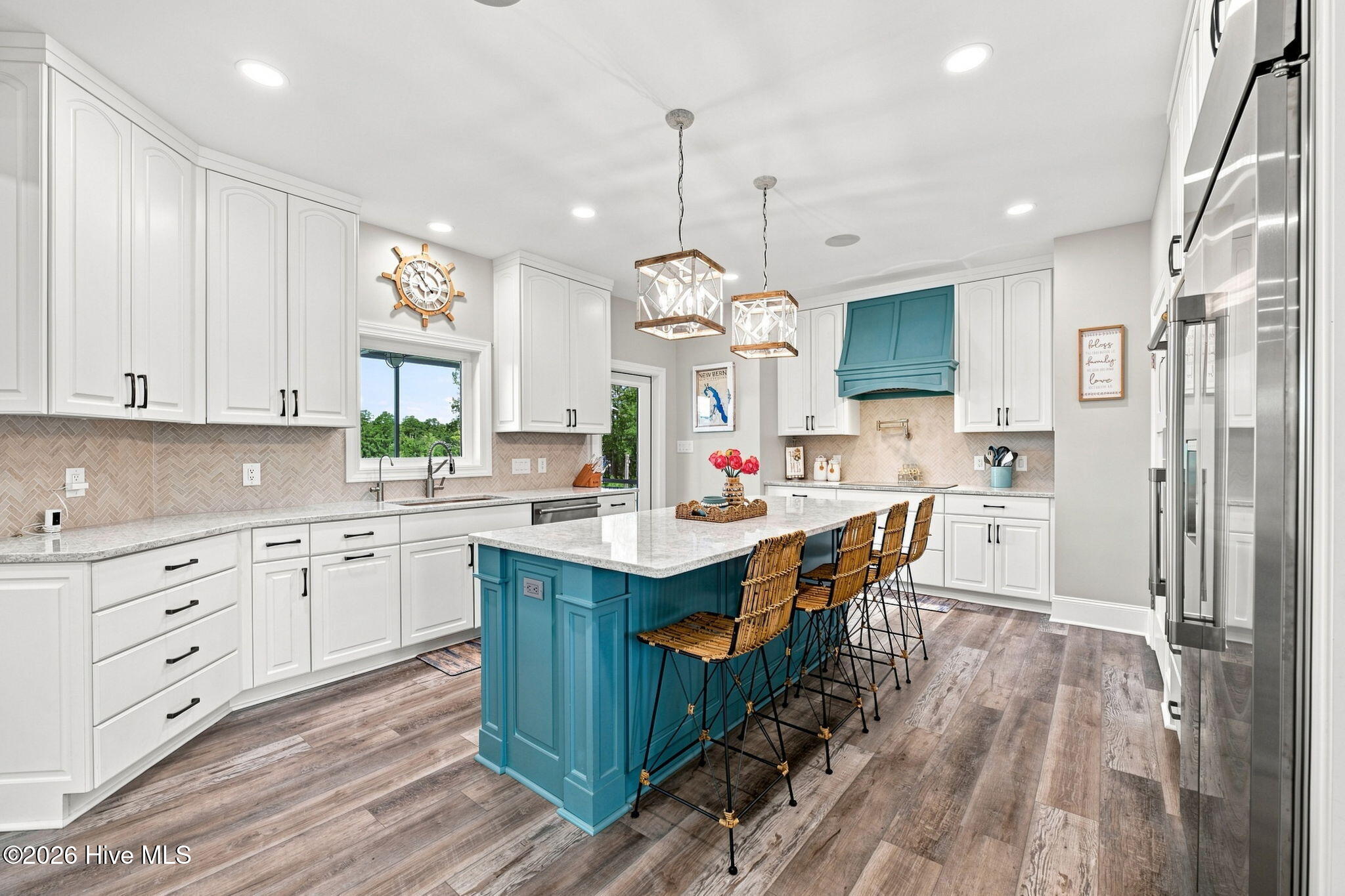 Kitchen with a turquoise island and range hood, white cabinetry, woven bar stools, and stainless steel appliances.