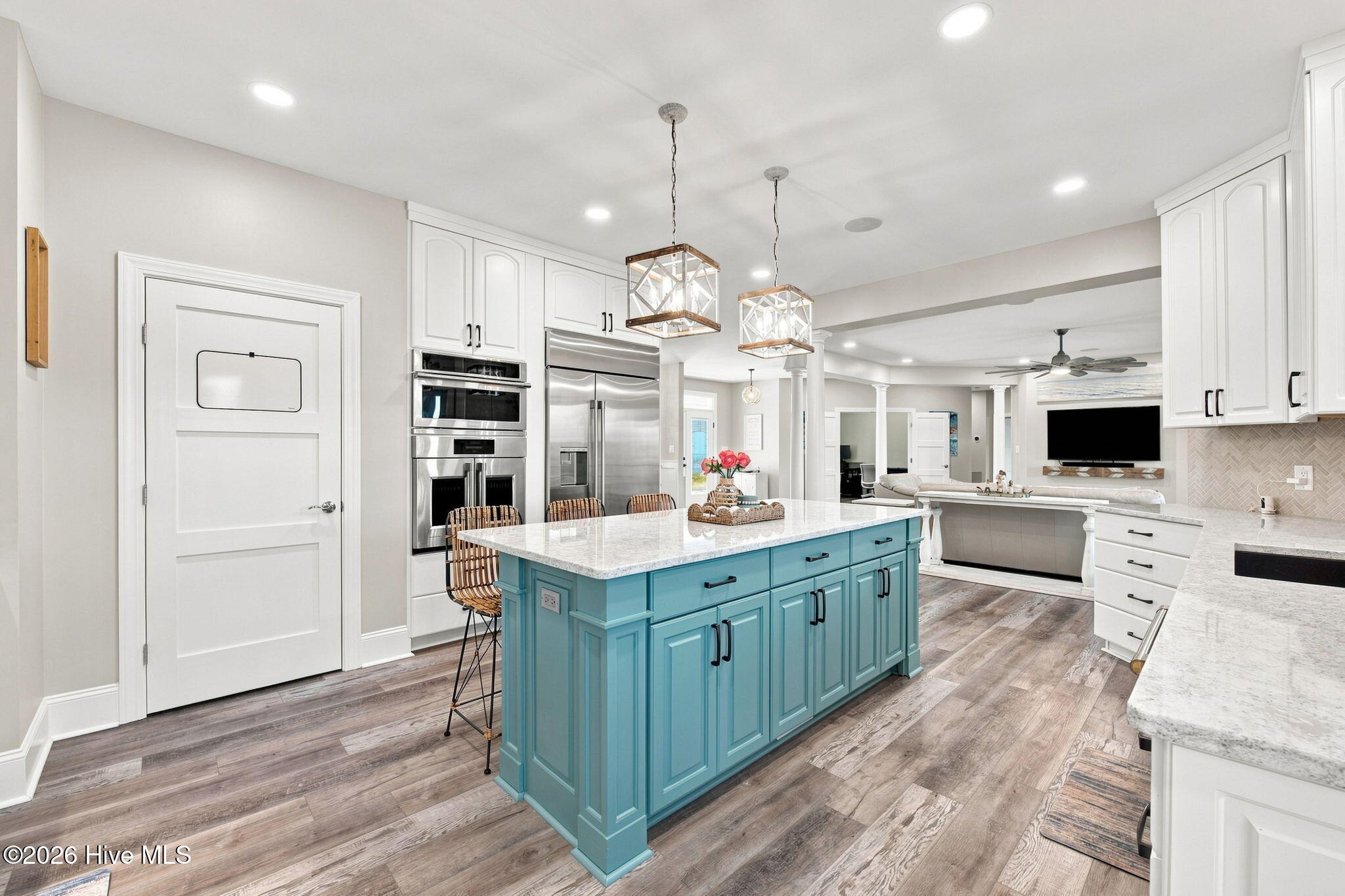 Open-plan kitchen with a turquoise island, white cabinetry, stainless steel appliances, and pendant lights.