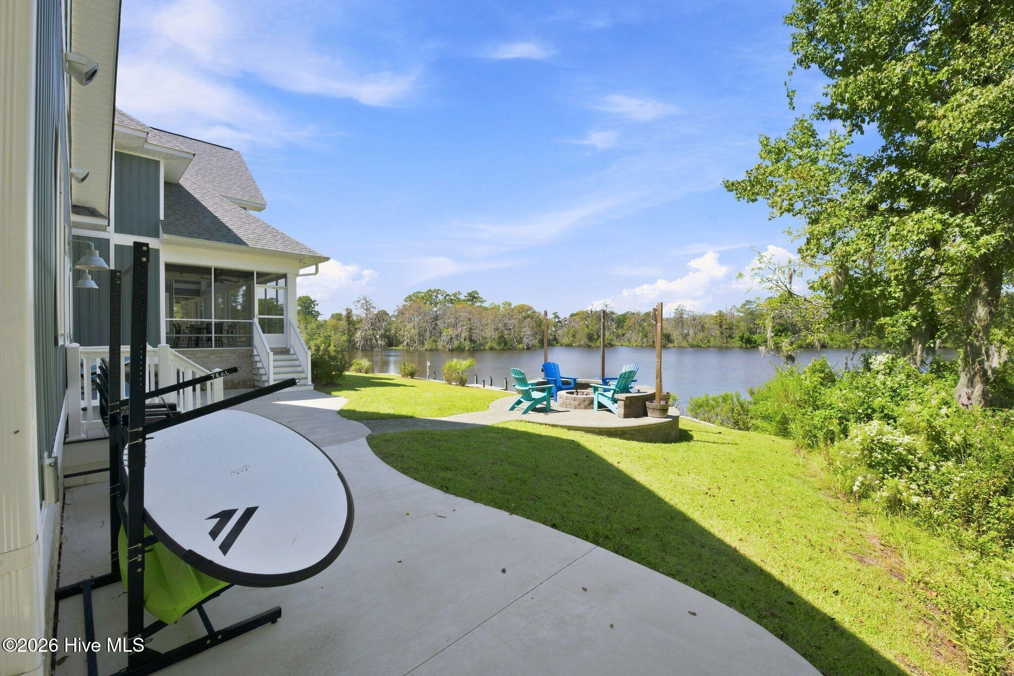 Waterfront backyard with a concrete patio, fire pit seating, screened porch, and paddleboard rack.