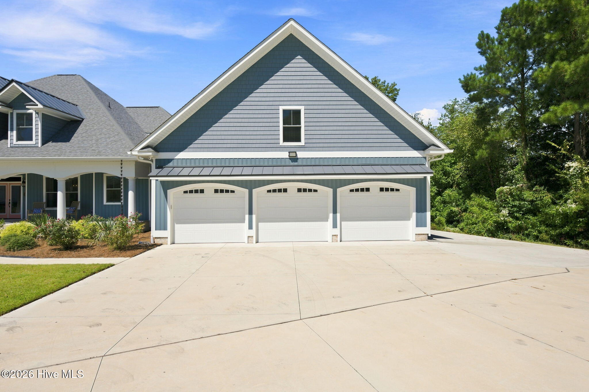 Blue-gray house with three-car garage, steep gable, and broad concrete driveway.