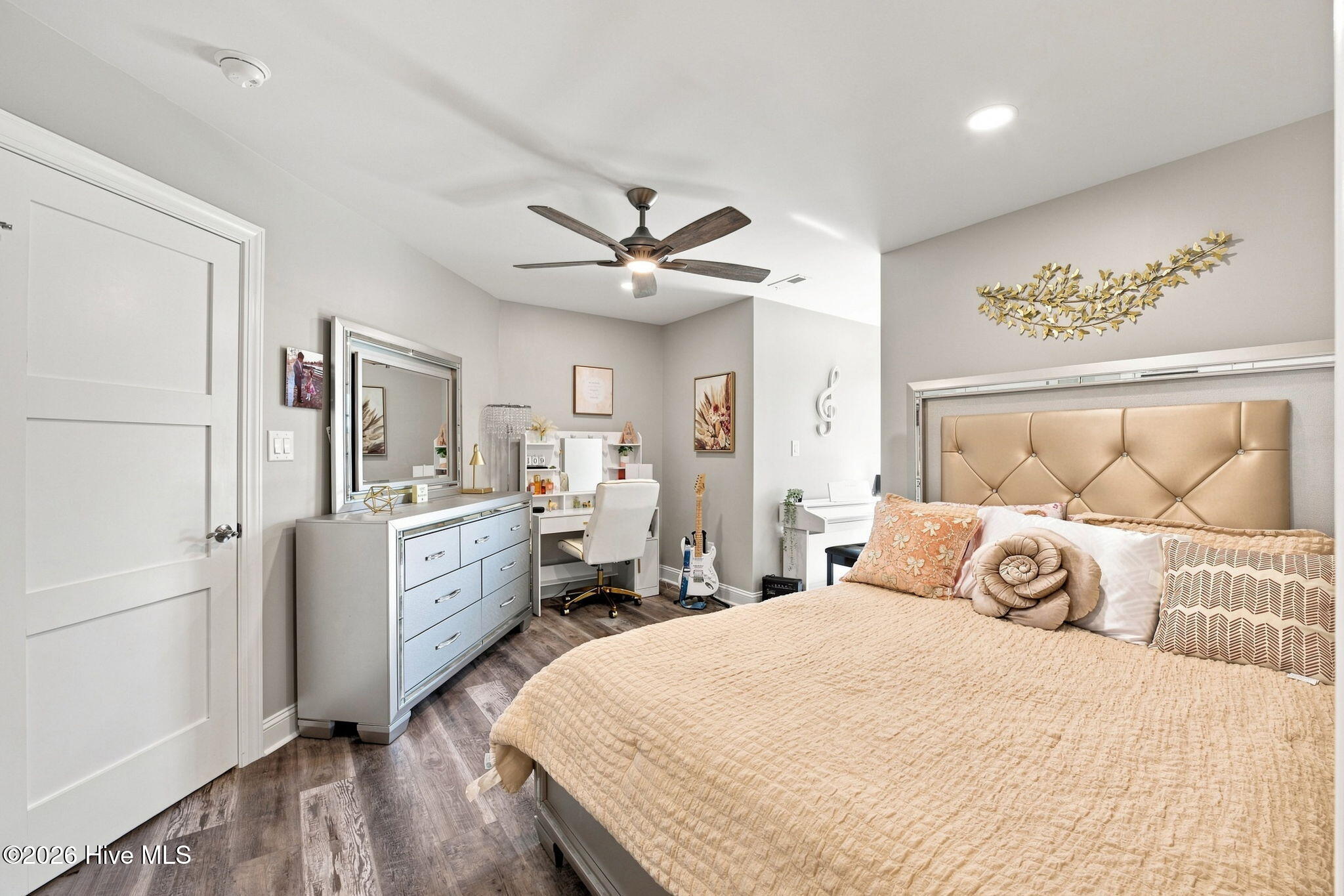 Bedroom with a tan tufted headboard, peach bedding, vanity, and guitar.