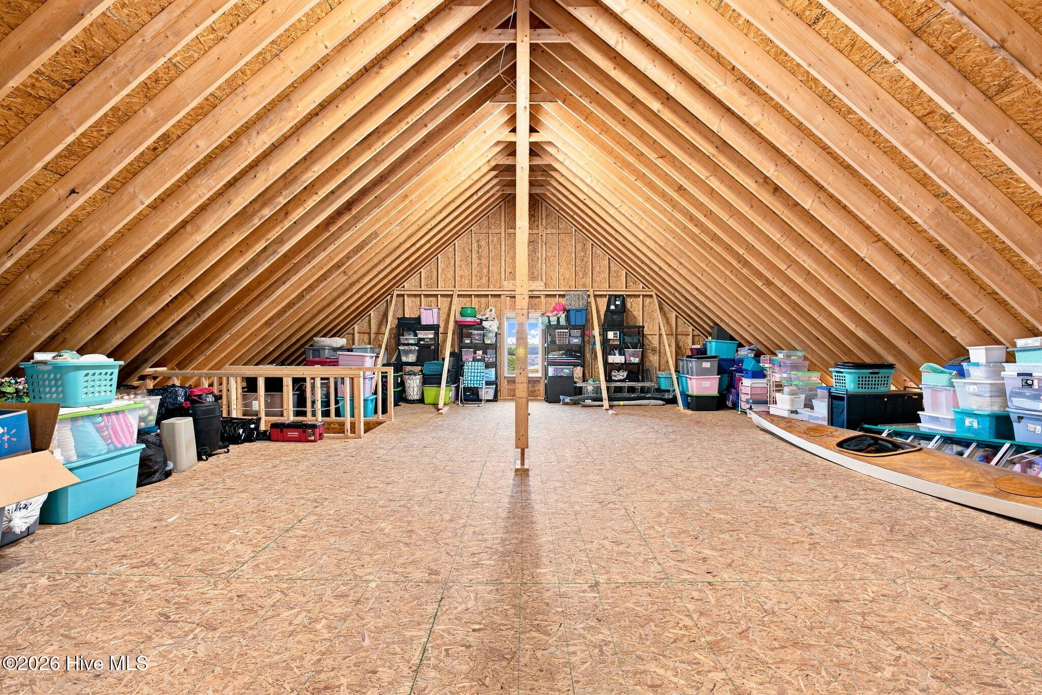 Unfinished attic with exposed rafters, a wide plywood floor, and storage bins along the sides.