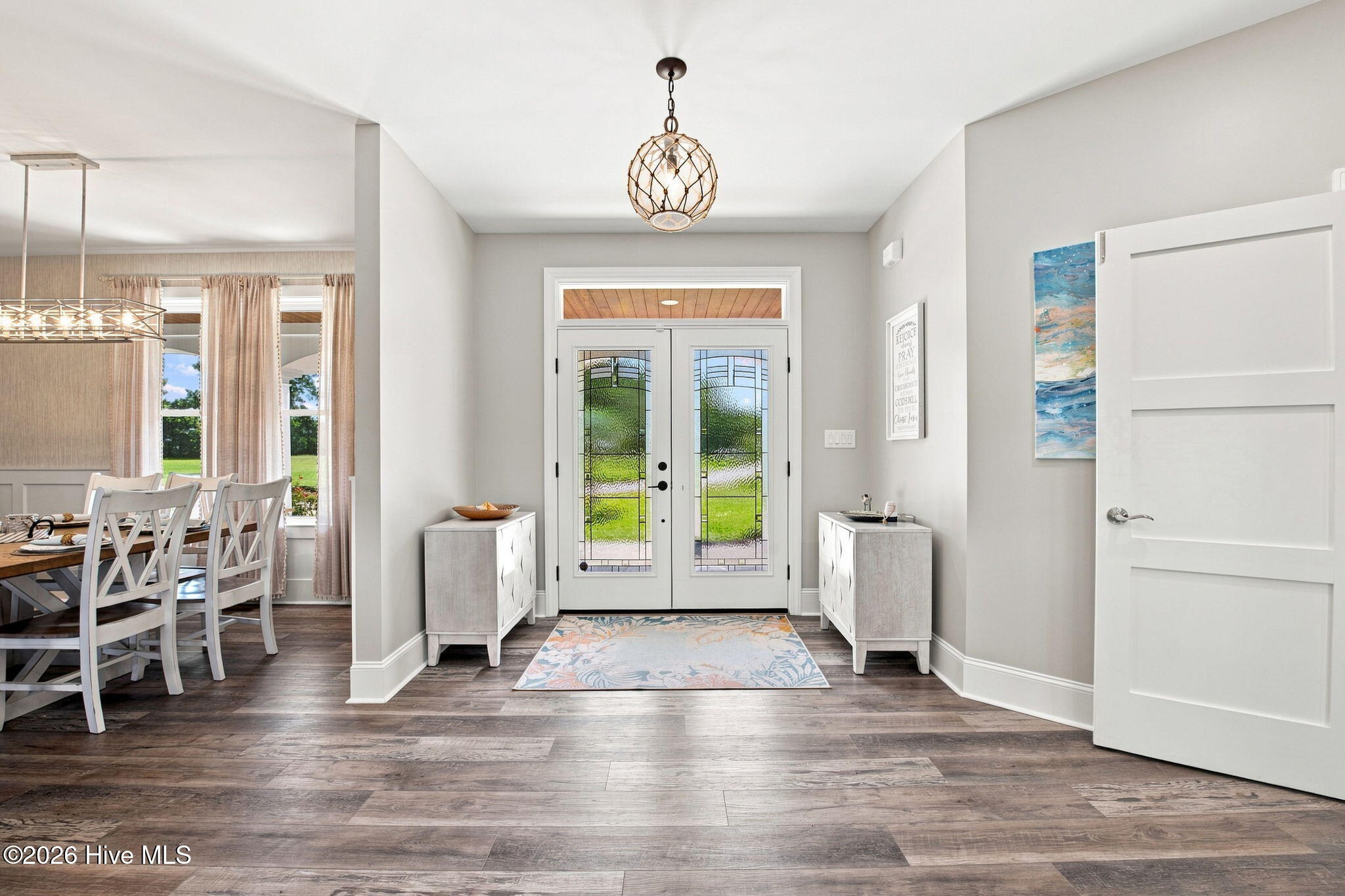 Foyer with patterned glass double doors, matching console cabinets, and a colorful rug beside the dining area.