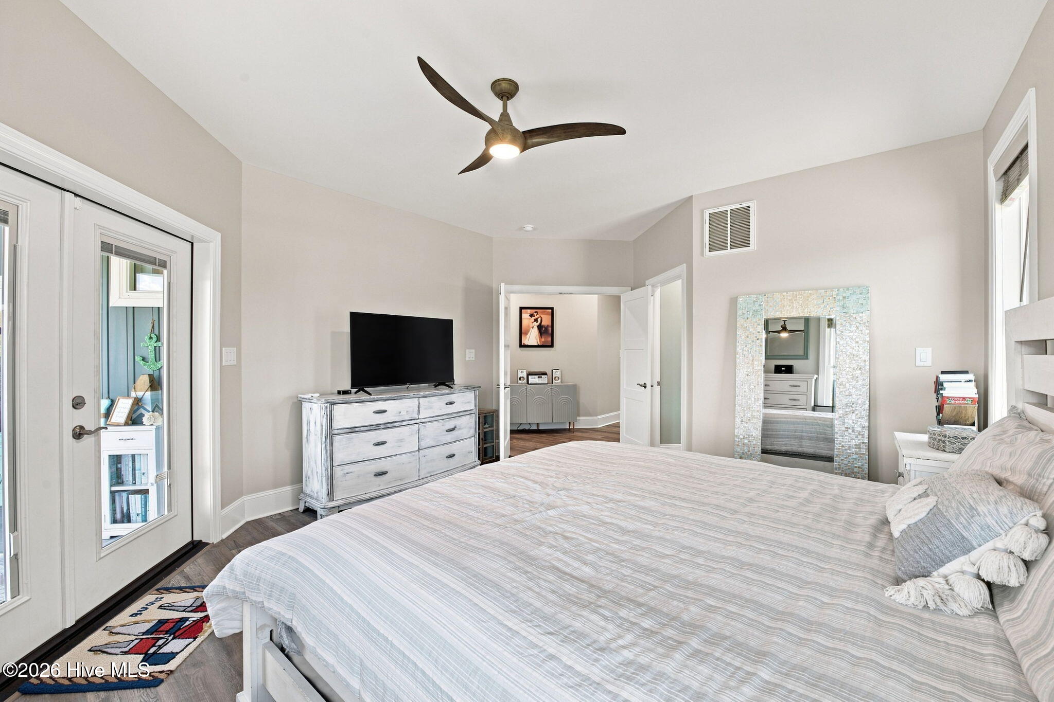Furnished bedroom with a large bed, ceiling fan, television, and mirrored closet doors.