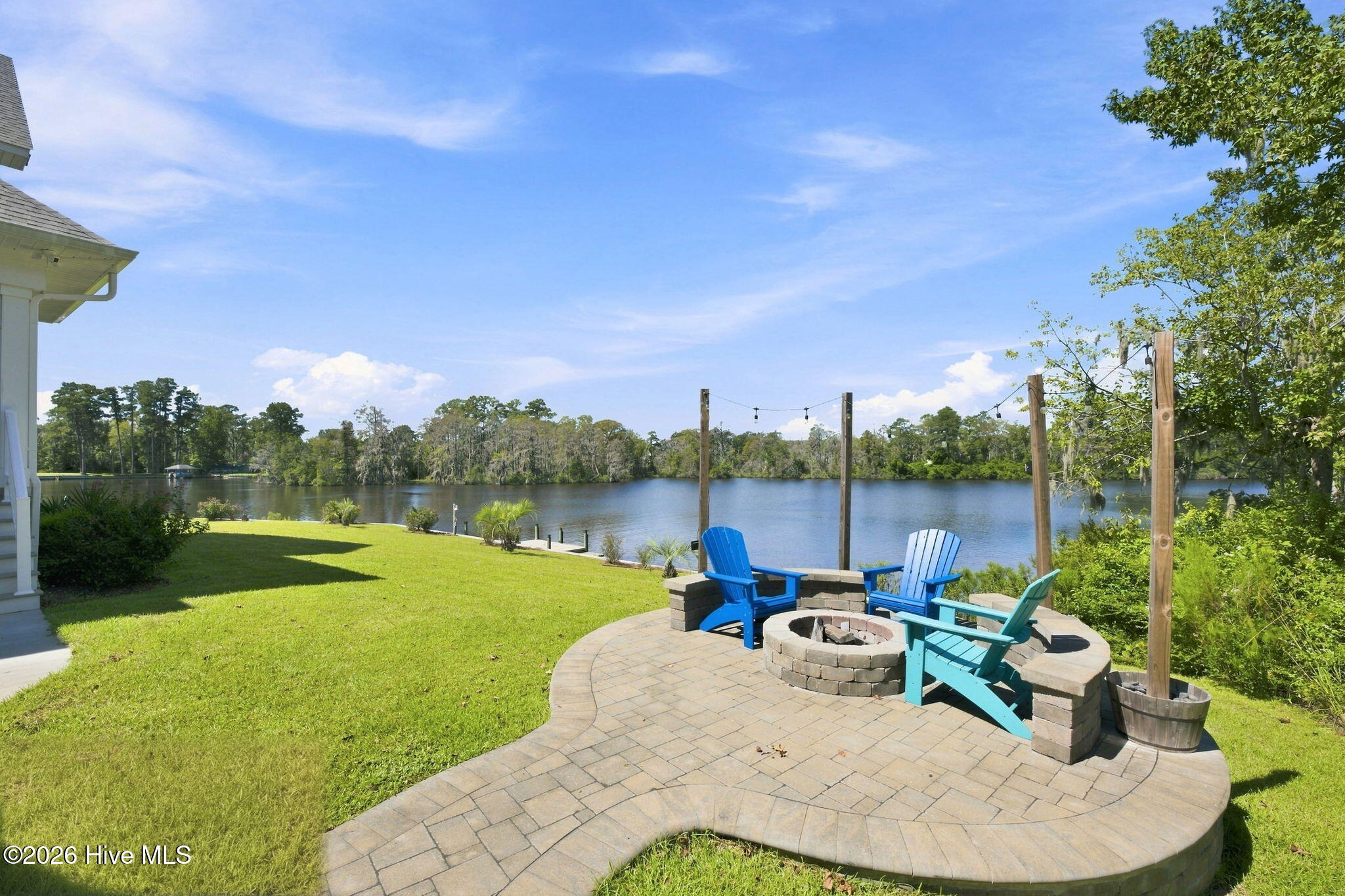Waterfront patio with a stone fire pit and colorful Adirondack chairs overlooking the river.