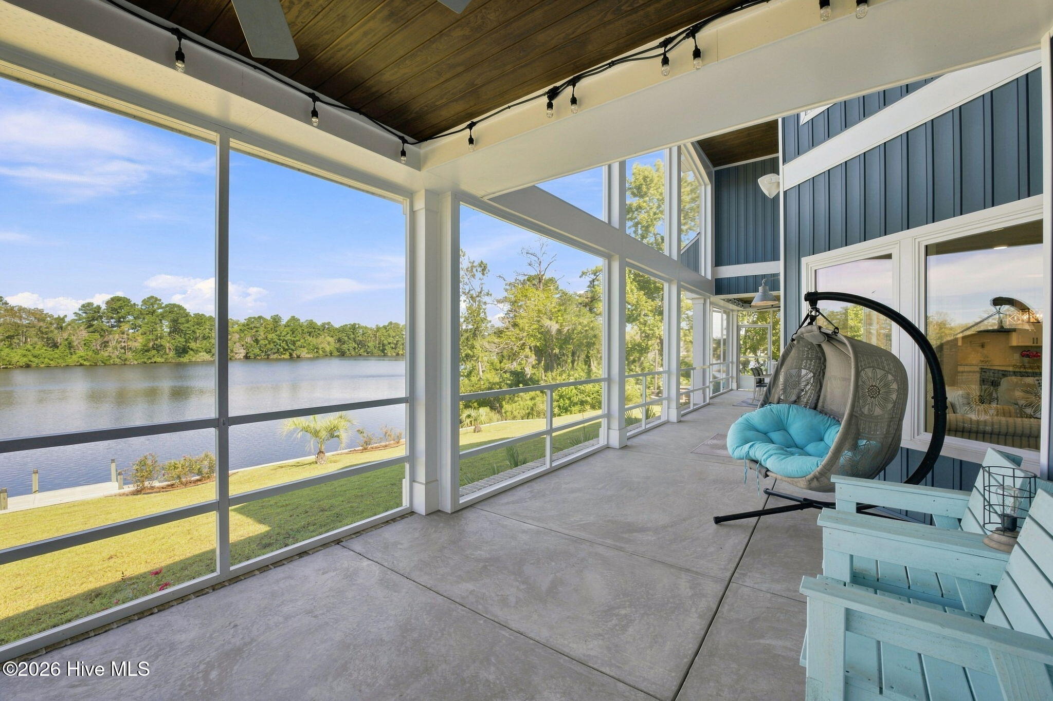 Screened porch with a hanging chair and Adirondack chairs overlooking a lake.