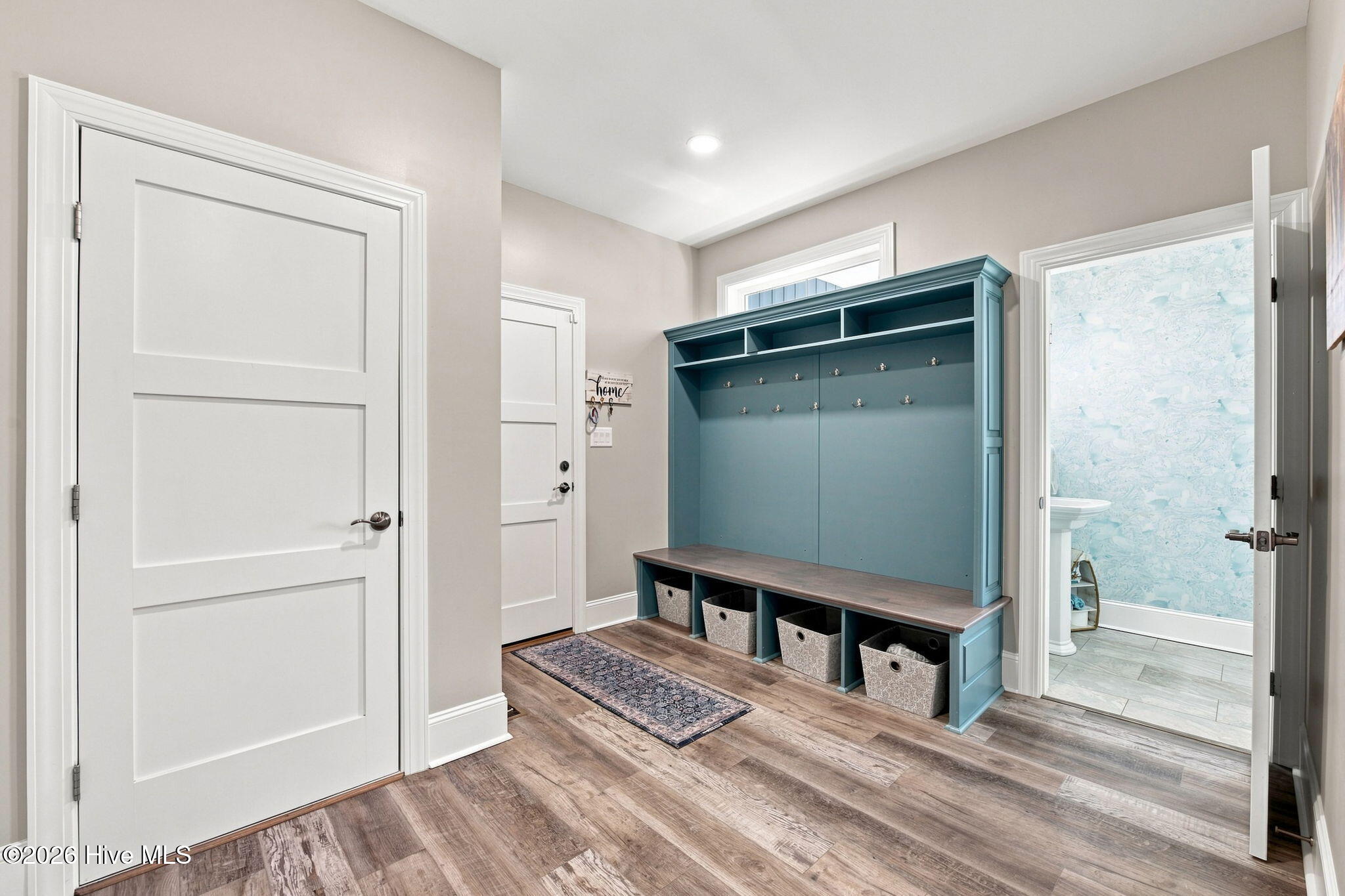 Mudroom with a teal built-in bench, coat hooks, cubbies, and storage baskets beside an open bathroom doorway.