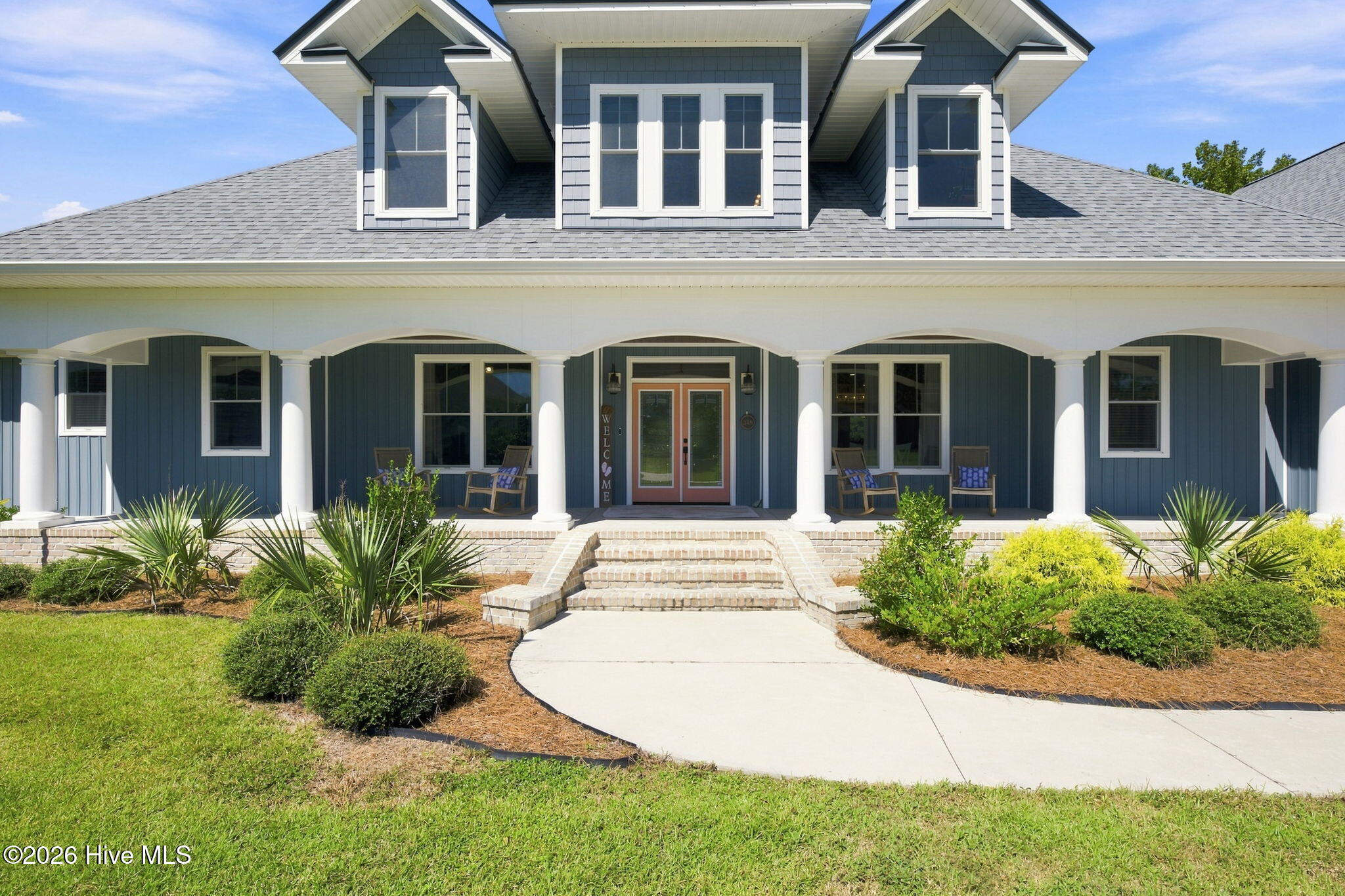 Blue-gray two-story home with upper dormers, a columned porch, brick steps, and landscaped front beds.