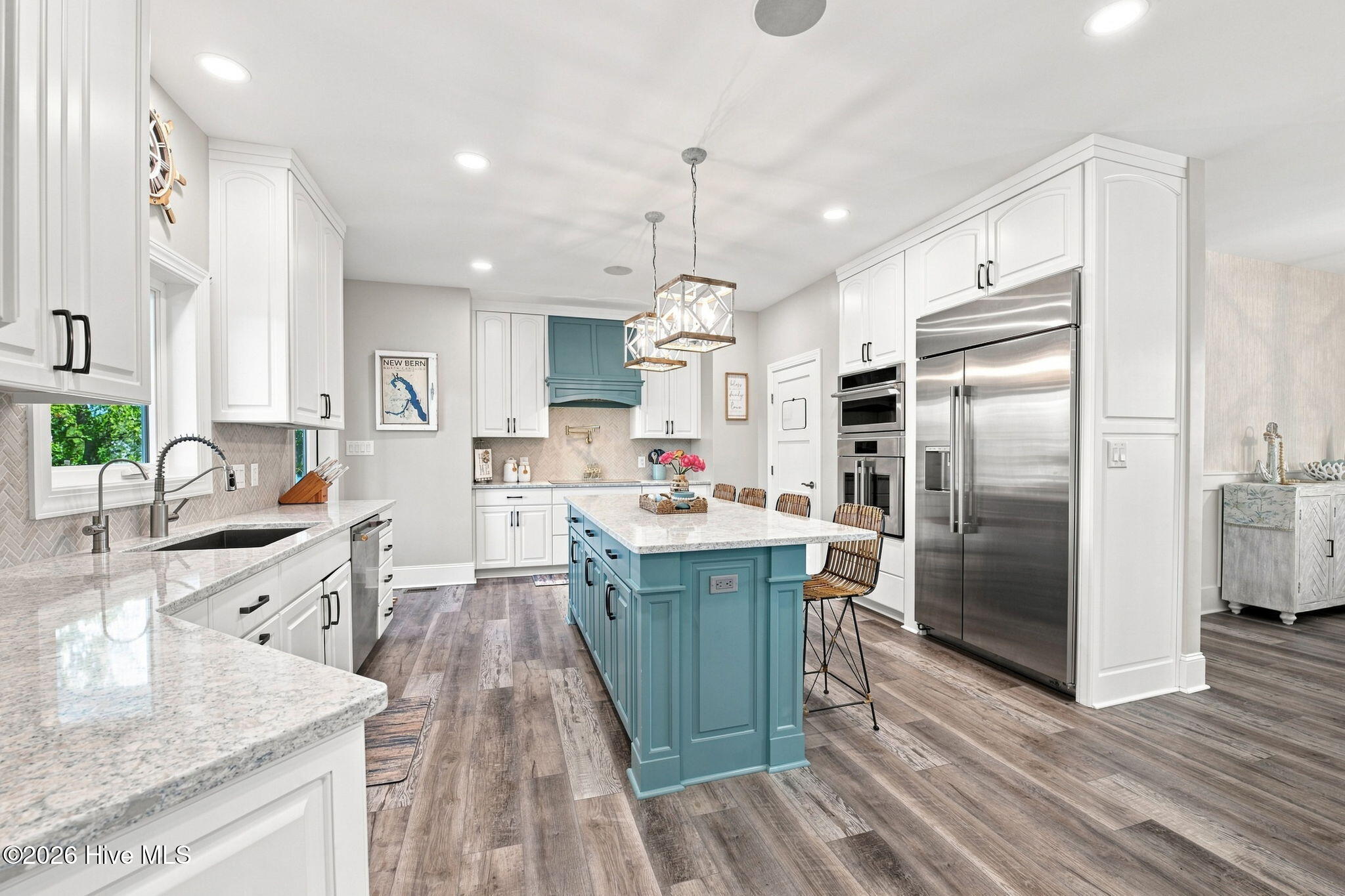 Kitchen with a teal-blue island and range hood, white cabinets, stone counters, and stainless steel appliances.
