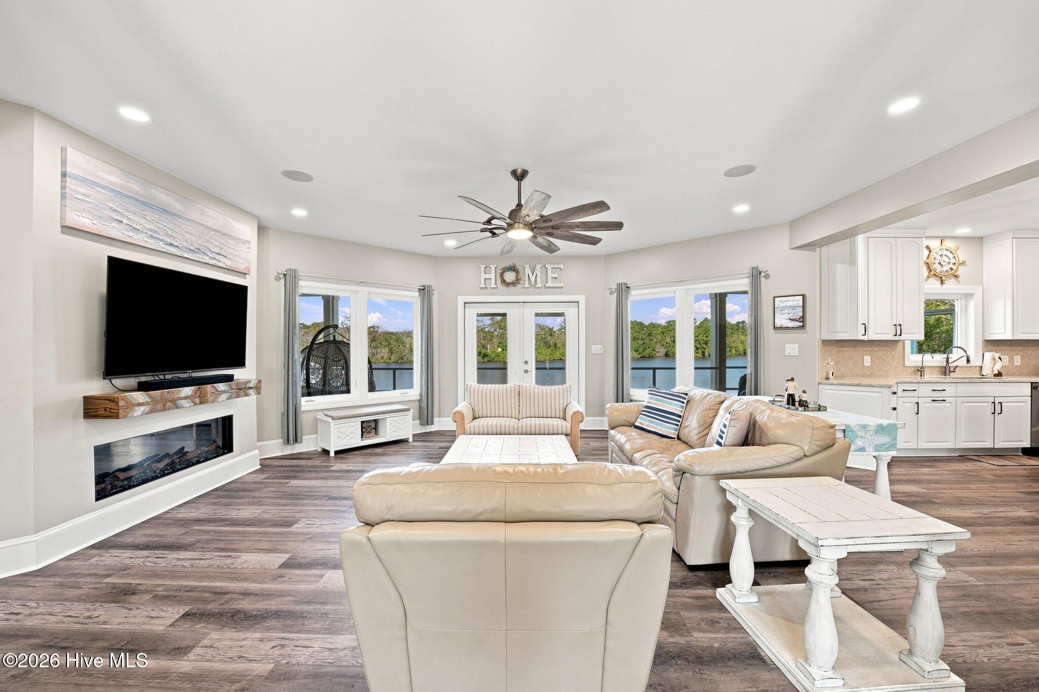 Furnished living room with a fireplace, adjoining kitchen, and lake views through large windows.