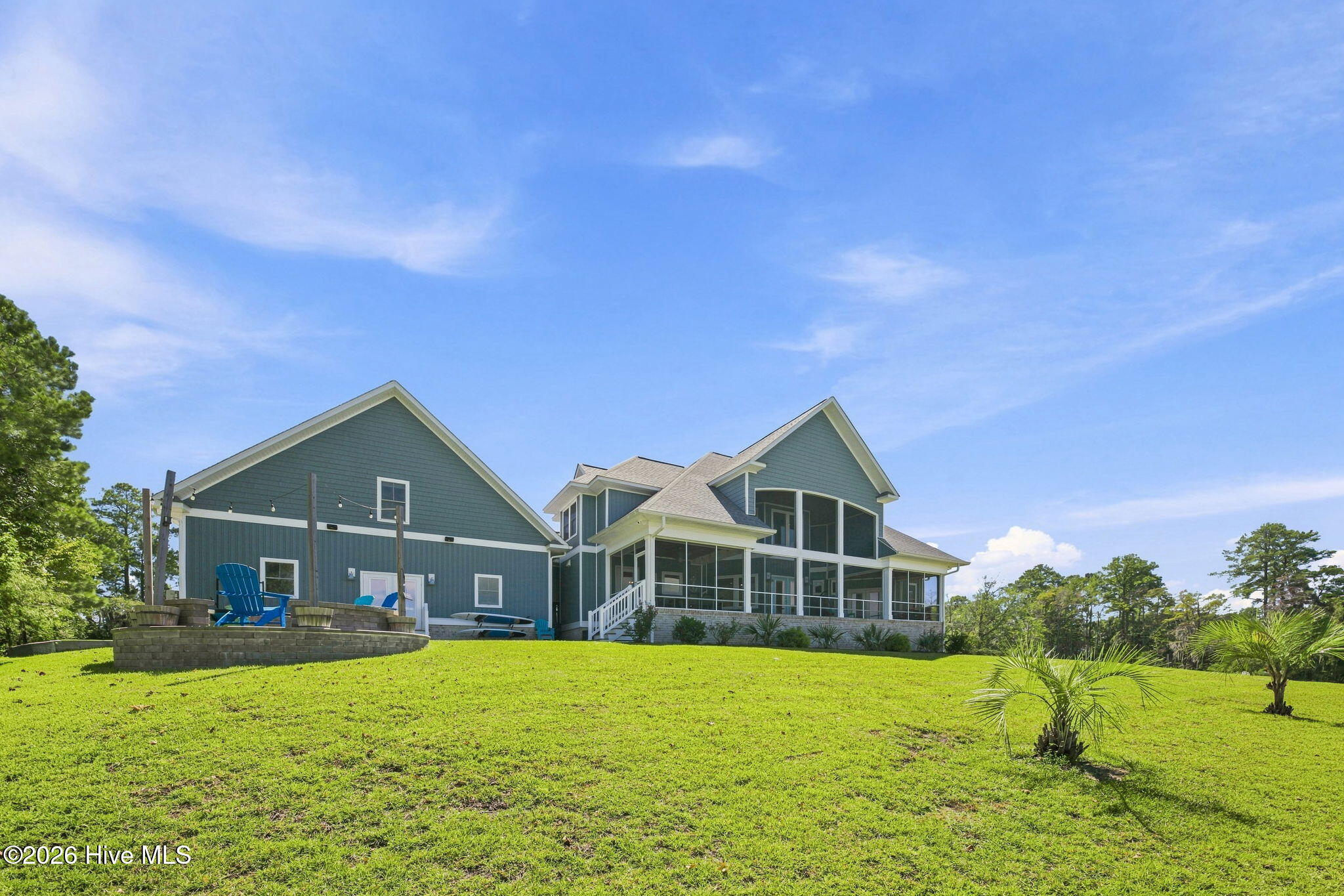 Blue-gray home with a screened porch, raised patio, and broad green lawn.