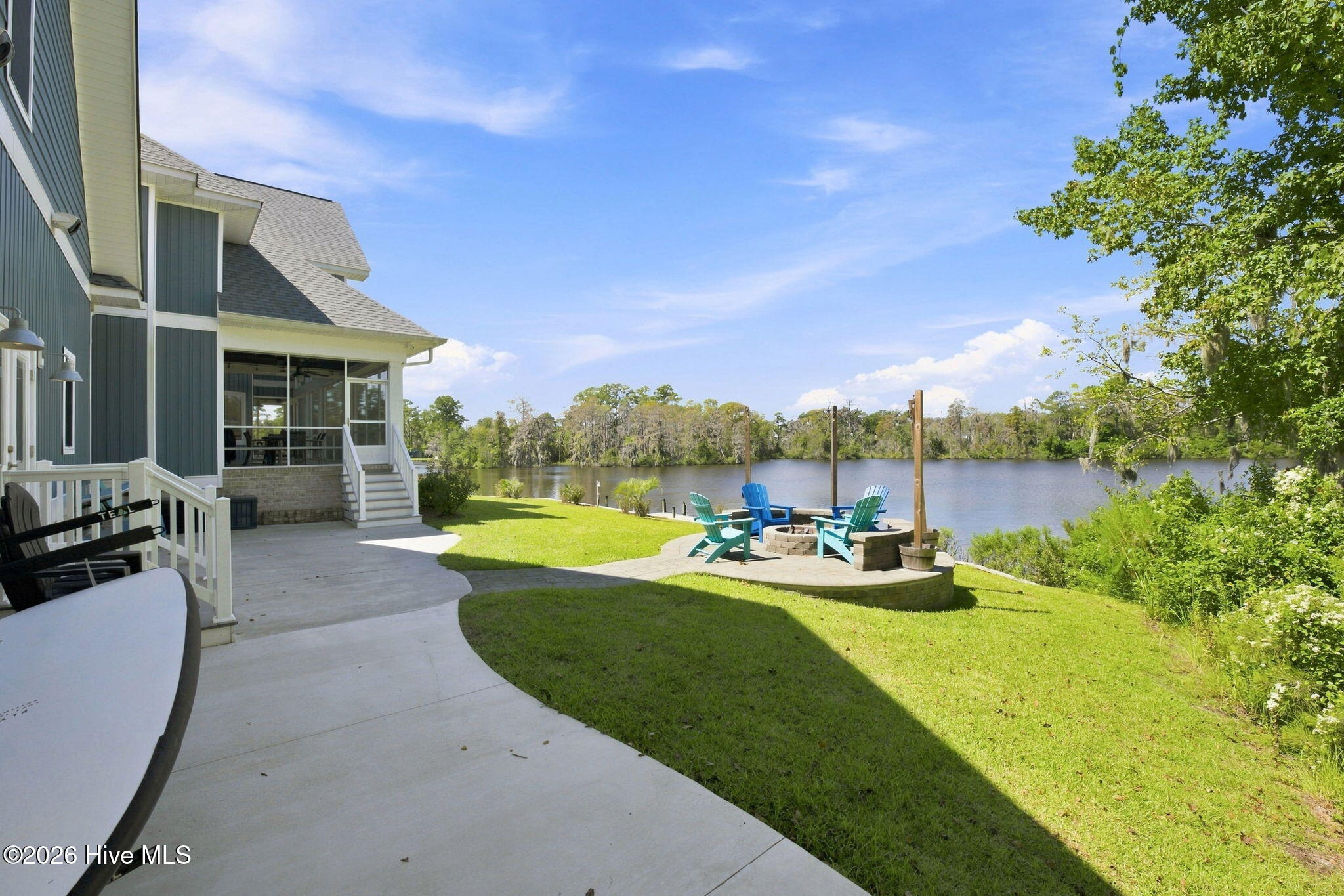House patio and lawn beside a river, with colorful Adirondack chairs around a fire pit.