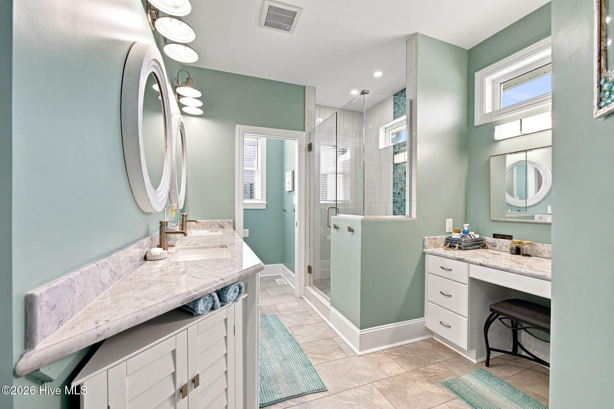 Bathroom with a marble double vanity, round mirrors, and glass shower with blue tile accents.