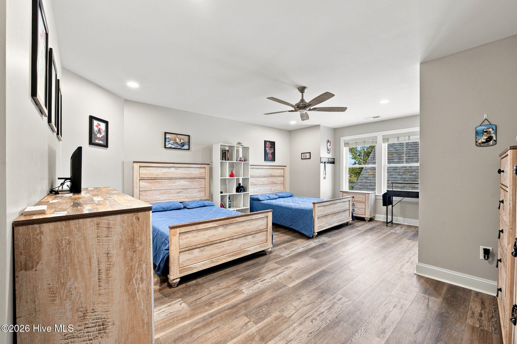Bedroom with two blue-covered beds, rustic wood furniture, and large windows.