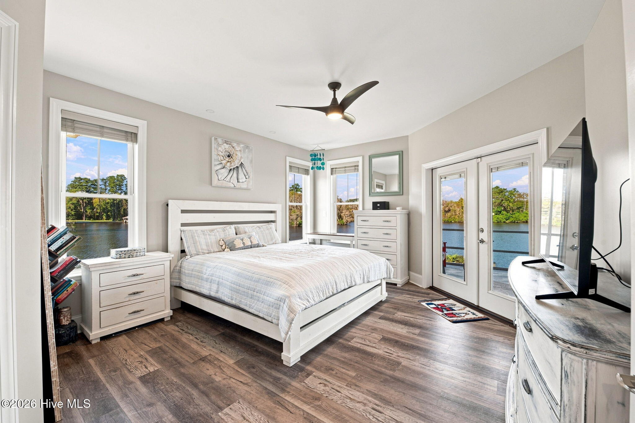 Furnished bedroom with a white bed and windows and glass doors overlooking the water.