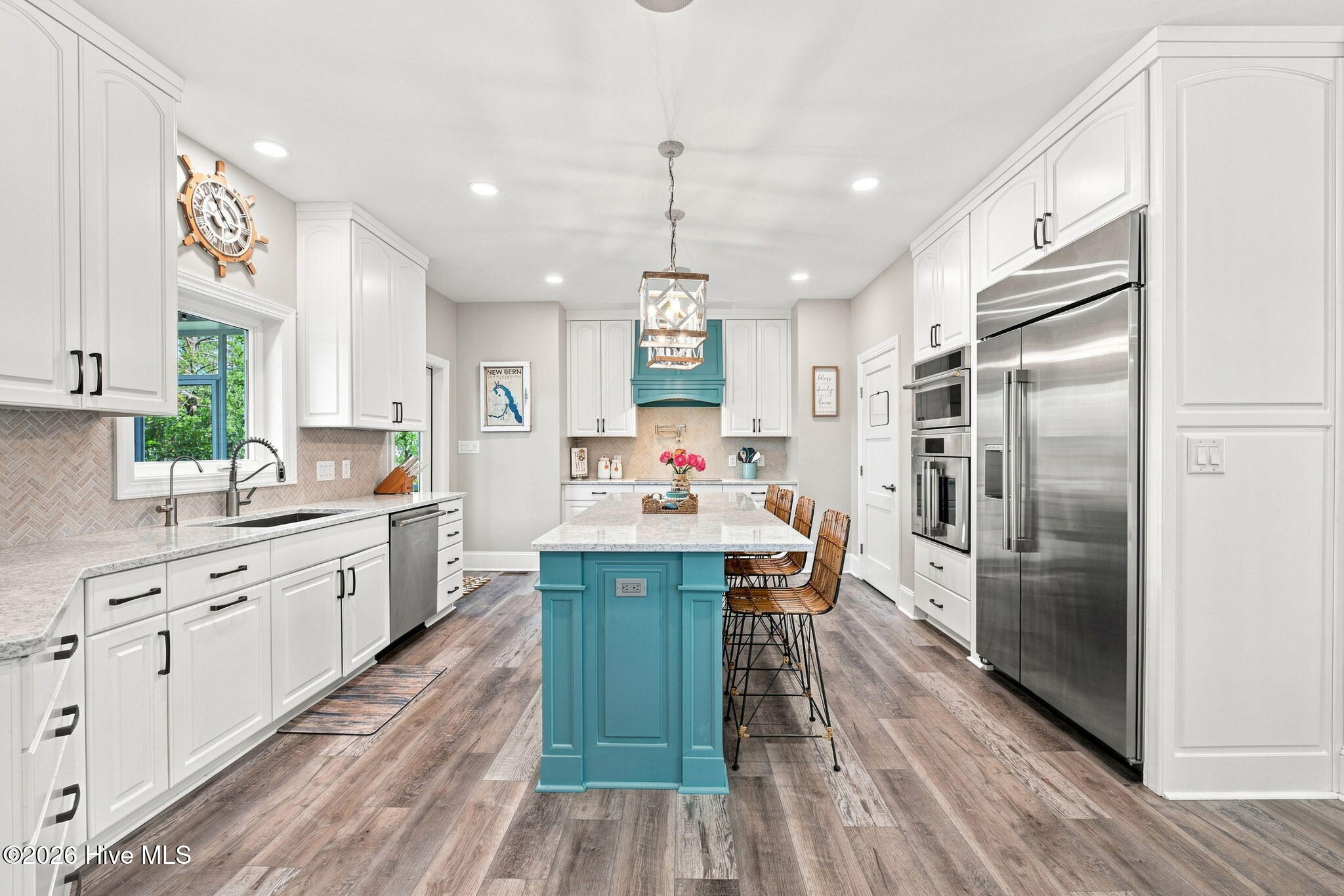 Bright kitchen with a turquoise island, white cabinetry, stainless steel appliances, and woven bar stools.